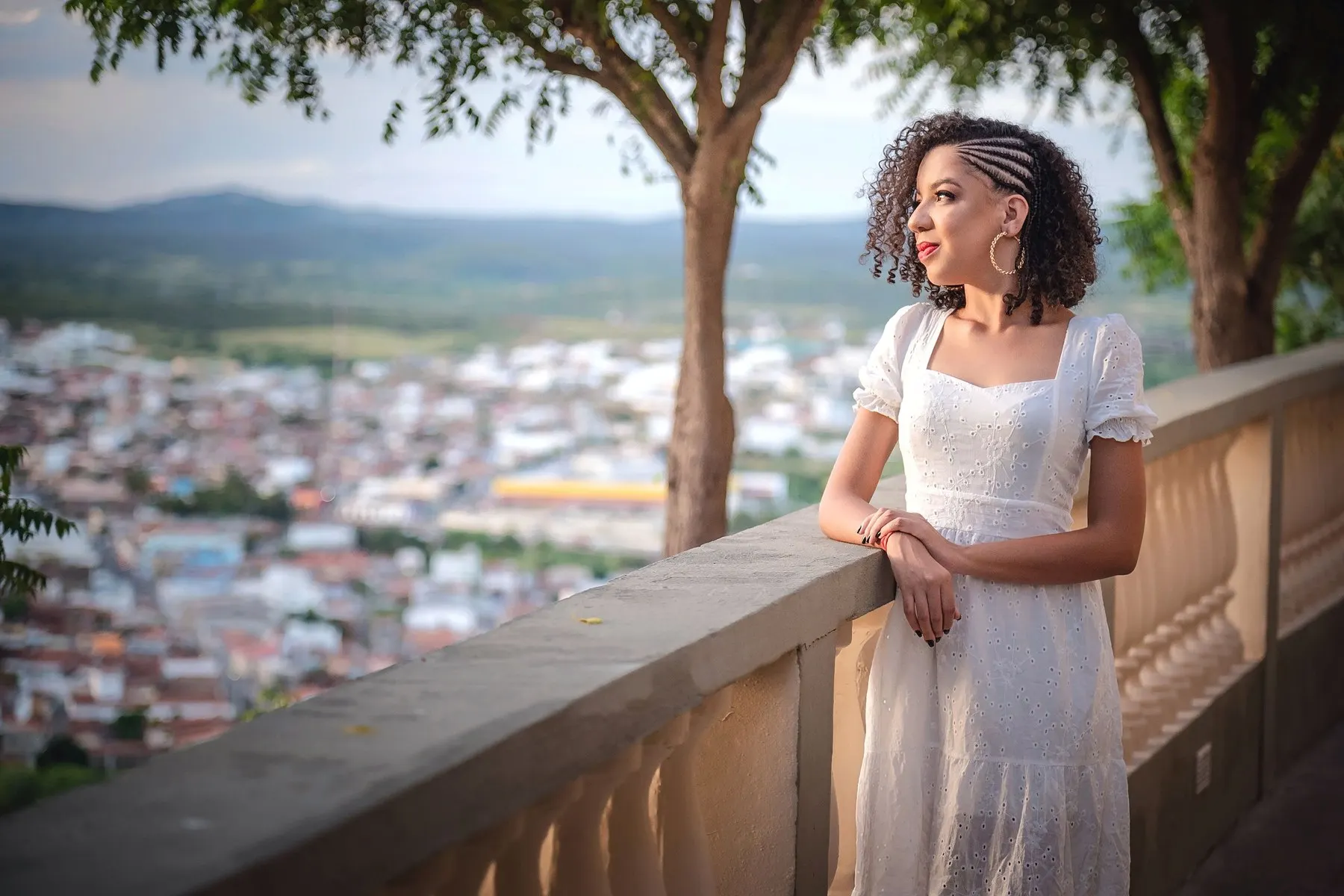 Layse Naele de vestido branco em um mirante, com a cidade ao fundo